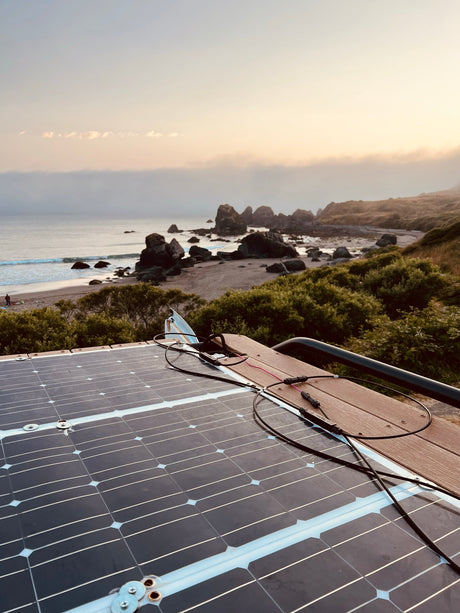 An rv rental's rooftop solar panels capture power overlooking a misty beach with sea stacks.
