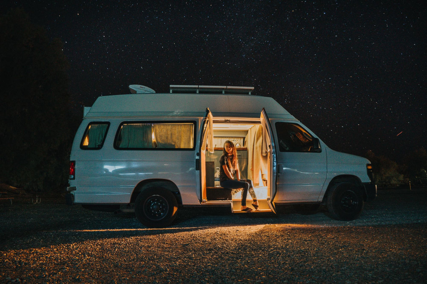 Starry night van life: Woman enjoys cozy RV rental interior under a brilliant, star-filled sky. Illuminated gravel road. — photo 3