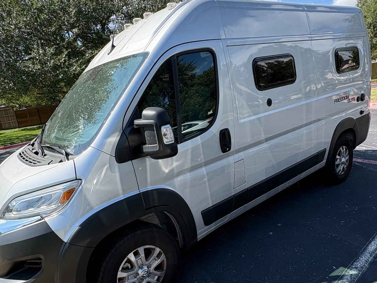  ready for your next RV rental adventure.|Silver Freedom Elite RV rental parked under a tree. Clear side view showing windows and a "2 Year Warranty" sticker.|Sleek white Freedom Elite Class B RV rental — photo 4