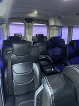 Luxurious RV rental interior: spacious black leather seating, white stitching, ambient lighting, and console with cup holders.