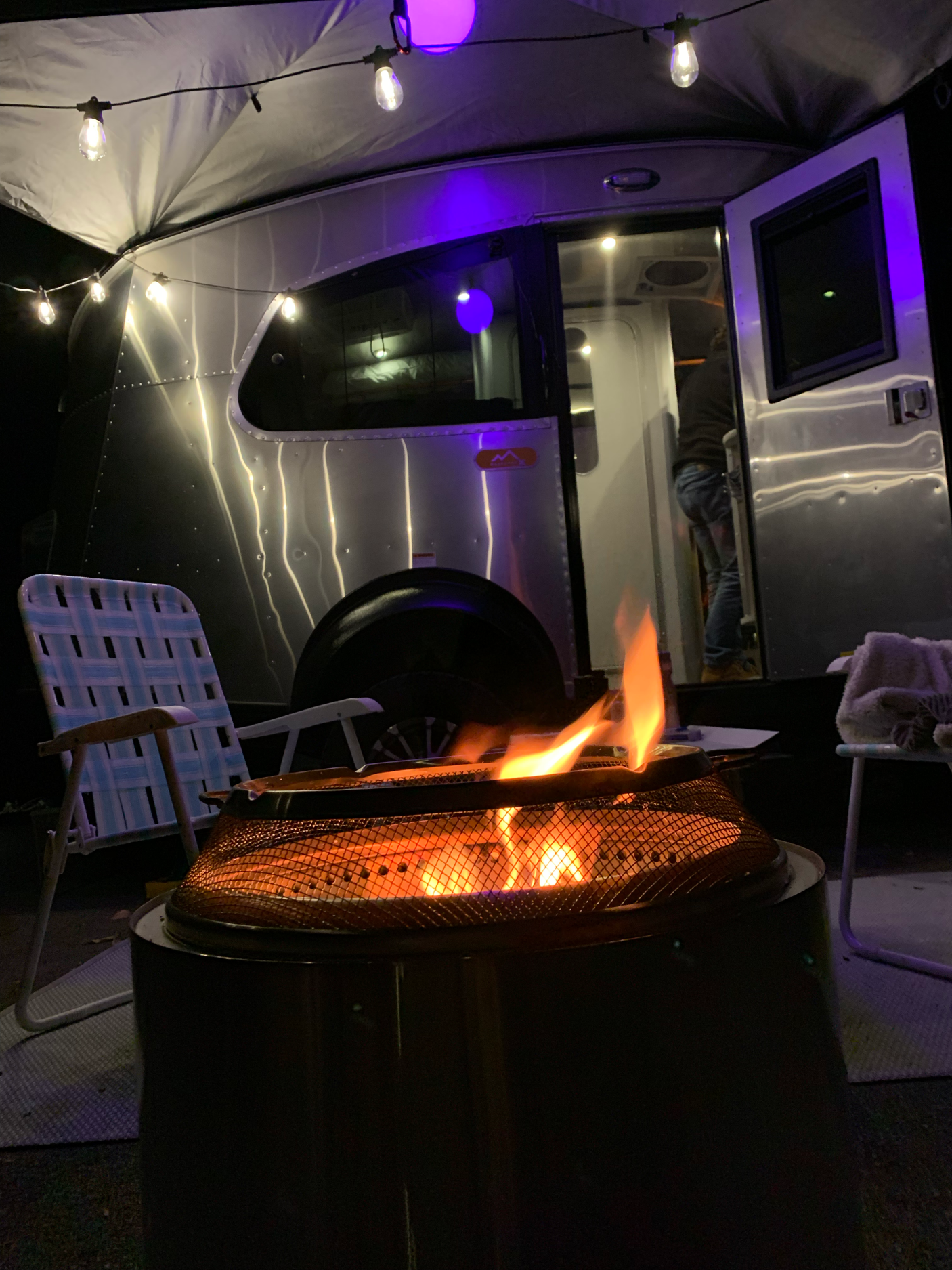 Cozy evening with a fire pit beside an RV rental, illuminated by string lights. Perfect for camping.