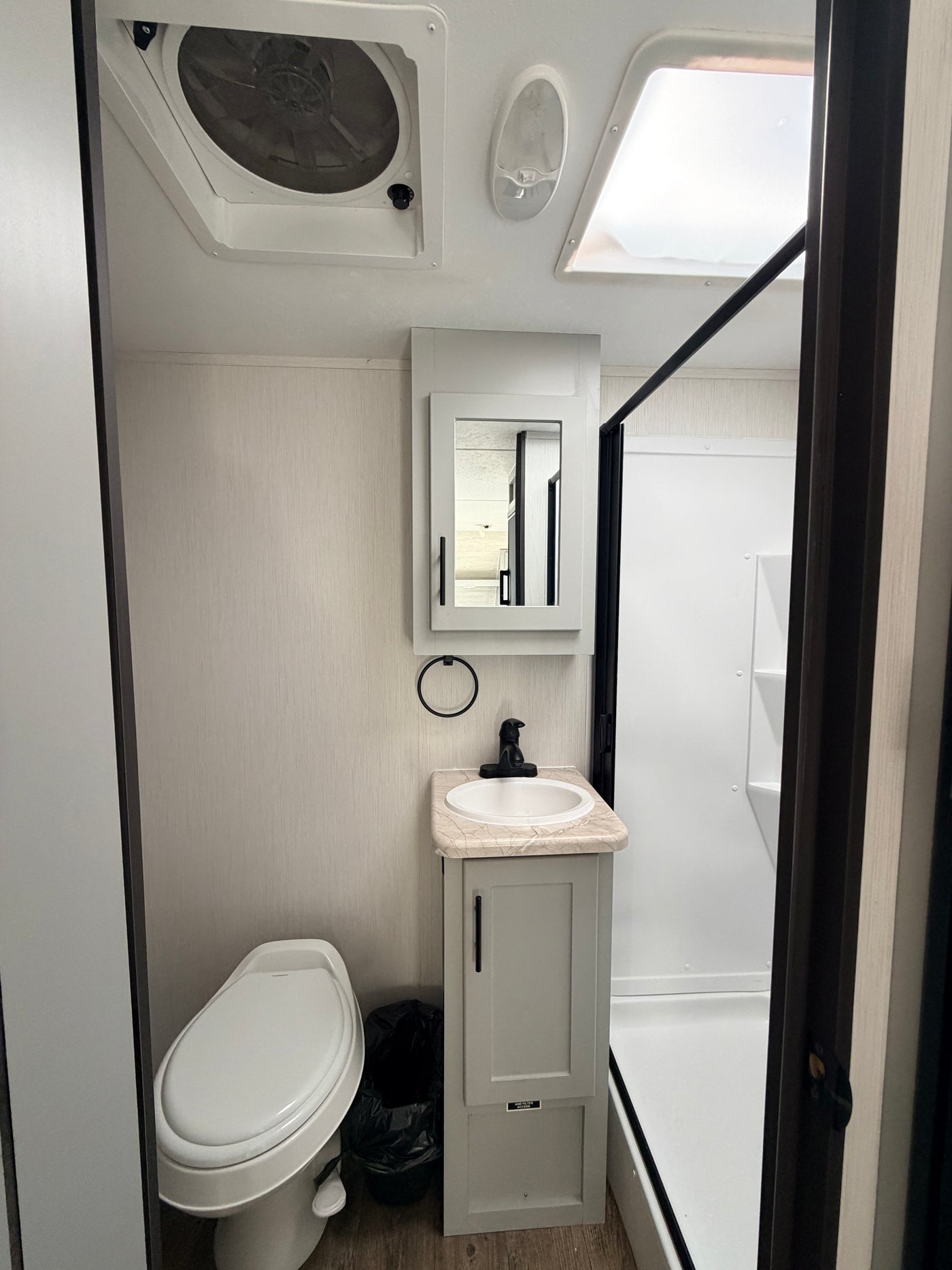 Compact RV rental bathroom with toilet, sink, shower, ceiling vent, and skylight, perfect for travel. — photo 7