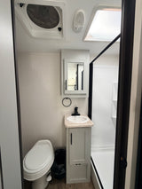 Compact RV rental bathroom with toilet, sink, shower, ceiling vent, and skylight, perfect for travel.