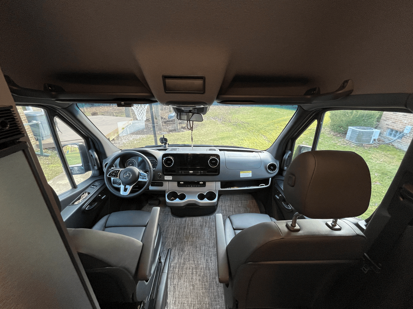 Spacious RV rental cockpit with Mercedes-Benz steering wheel, comfortable front seats, and a clear view out the windshield.