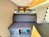 This RV rental interior features a cozy bed, modular seating, and compact kitchen. Ideal for road trip adventures.