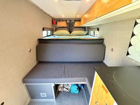 This RV rental interior features a cozy bed, modular seating, and compact kitchen. Ideal for road trip adventures.