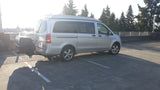 Silver high-roof camper van with a rear cargo box, perfect for an RV rental. Parked in a sunlit lot.