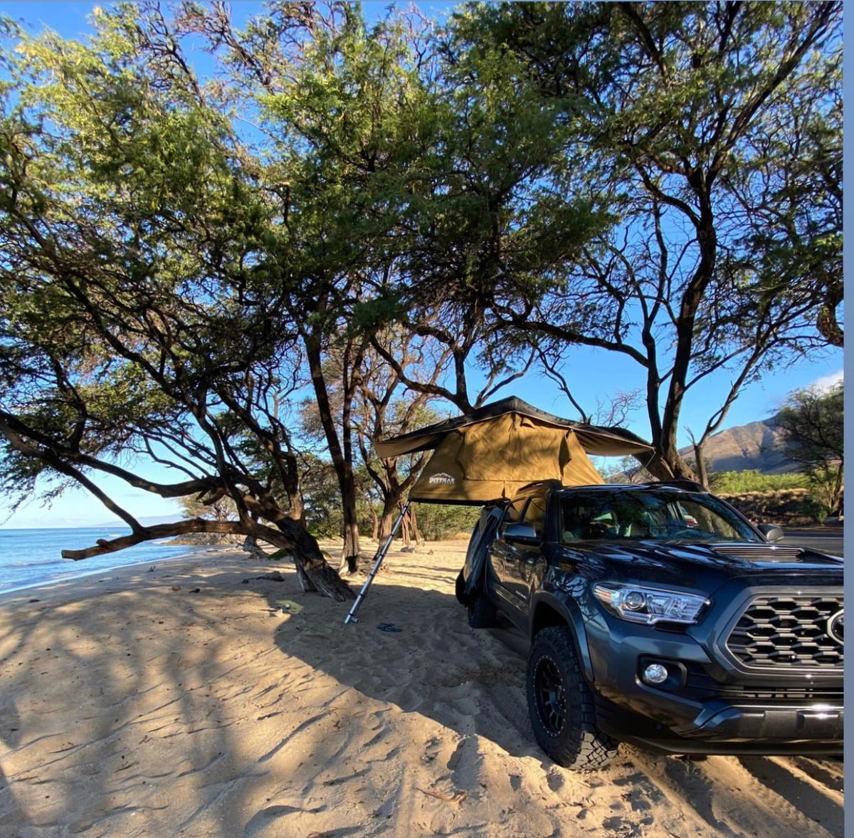 A pickup truck with an open rooftop tent is parked for beach camping under trees, a unique RV rental experience. — photo 2