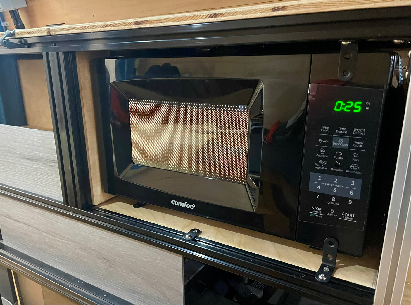 This black microwave oven, showing "0:25", is custom-installed in an RV rental, perfect for quick meals on the go.