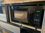This black microwave oven, showing "0:25", is custom-installed in an RV rental, perfect for quick meals on the go.