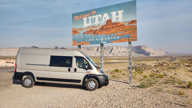 RV rental van next to the "Welcome to Utah" sign, showcasing scenic desert landscapes for a road trip adventure.