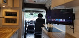 Inside an RV rental: a modern camper van interior with wooden counters, induction cooktop, wall-mounted TV, and driver's cabin view.