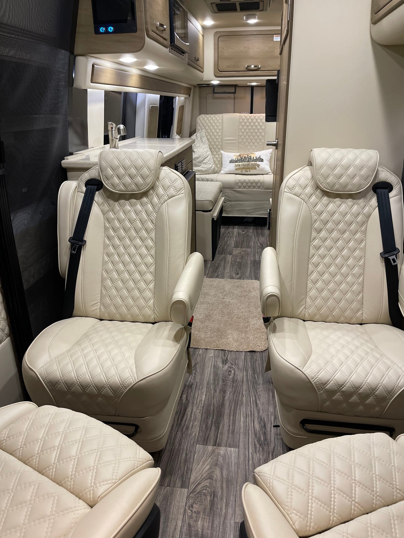 Spacious RV rental interior featuring cream quilted leather captain's chairs, a kitchenette, and wood-look flooring. — photo 12