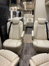 Spacious RV rental interior featuring cream quilted leather captain's chairs, a kitchenette, and wood-look flooring.