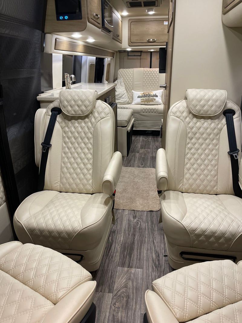 Spacious RV rental interior featuring cream quilted leather captain's chairs, a kitchenette, and wood-look flooring. — photo 12