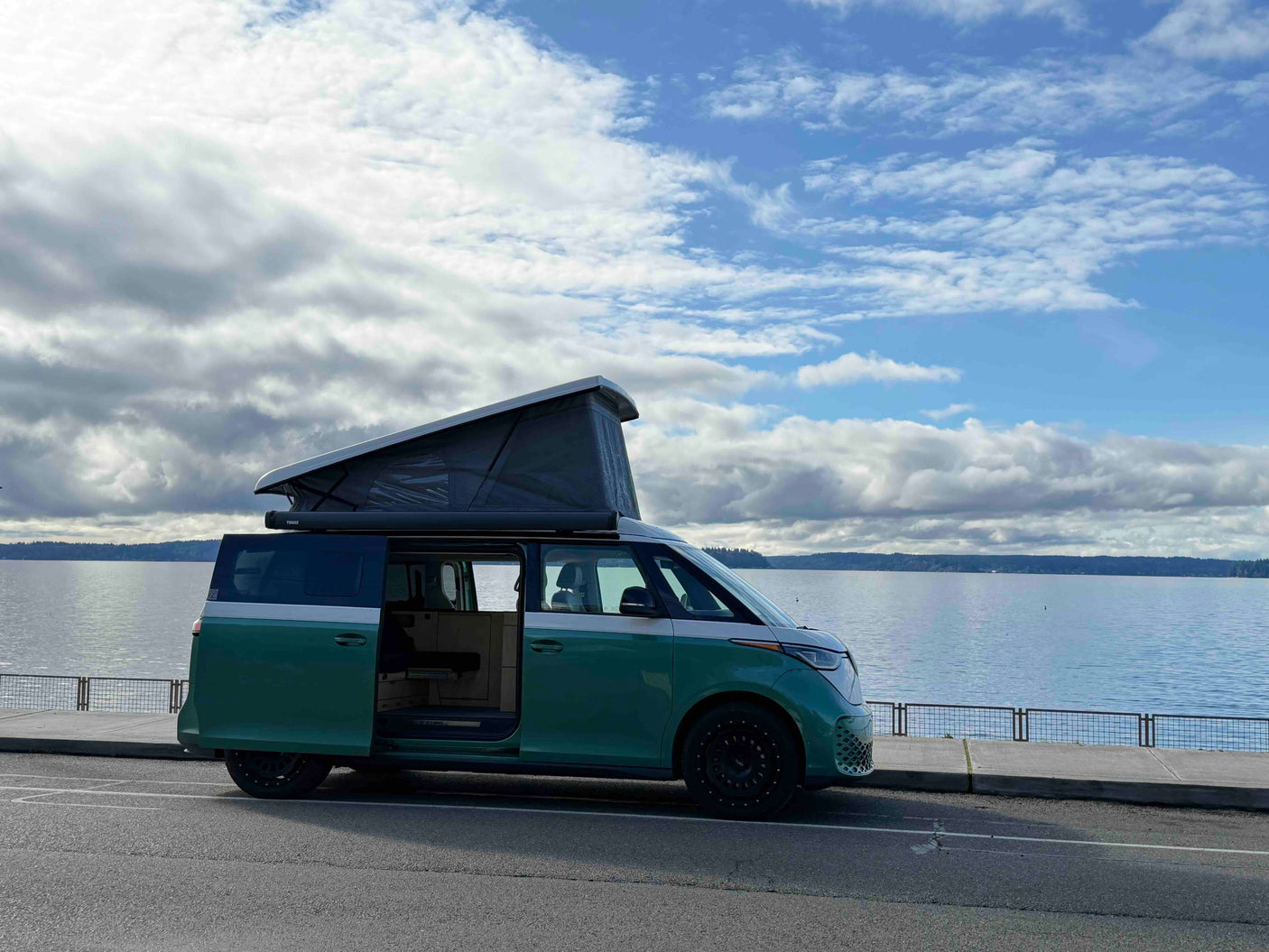 A green VW ID. Buzz camper van with pop-top by a scenic lake, ideal for your next rv rental adventure.