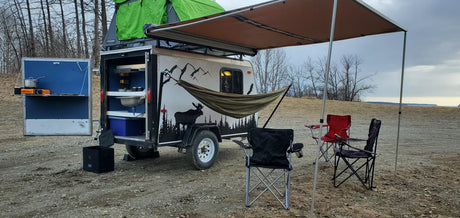 Custom camping trailer: green rooftop tent, outdoor kitchen, awning with chairs & hammock. Consider this unique RV rental for adventure.