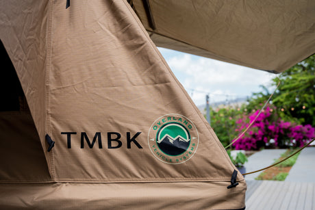 Close-up of a tan 'TMBK Overland Vehicle Systems' rooftop tent, ideal for an RV rental outdoor adventure.