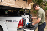 Man preparing food at a truck with a rooftop tent, resembling an RV rental setup for camping trips.