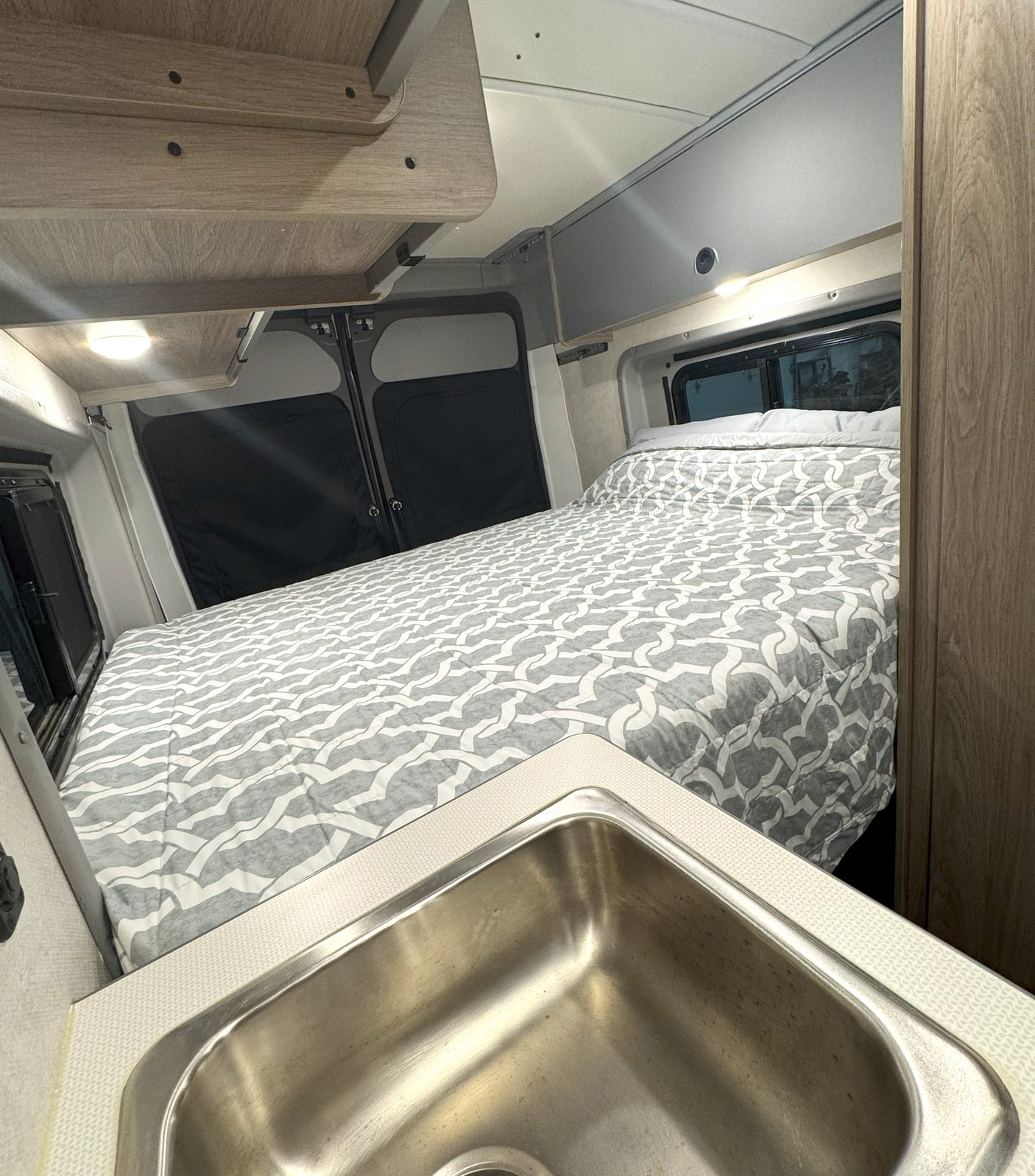 Cozy RV rental interior, showcasing a comfortable bed with a patterned comforter and a practical stainless steel kitchen sink.
