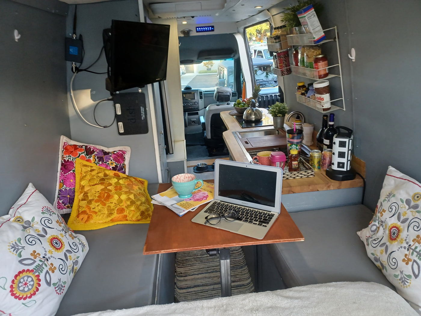 Cozy RV rental interior with a mobile office setup: laptop on table, kitchenette, and comfortable seating with pillows. — photo 9