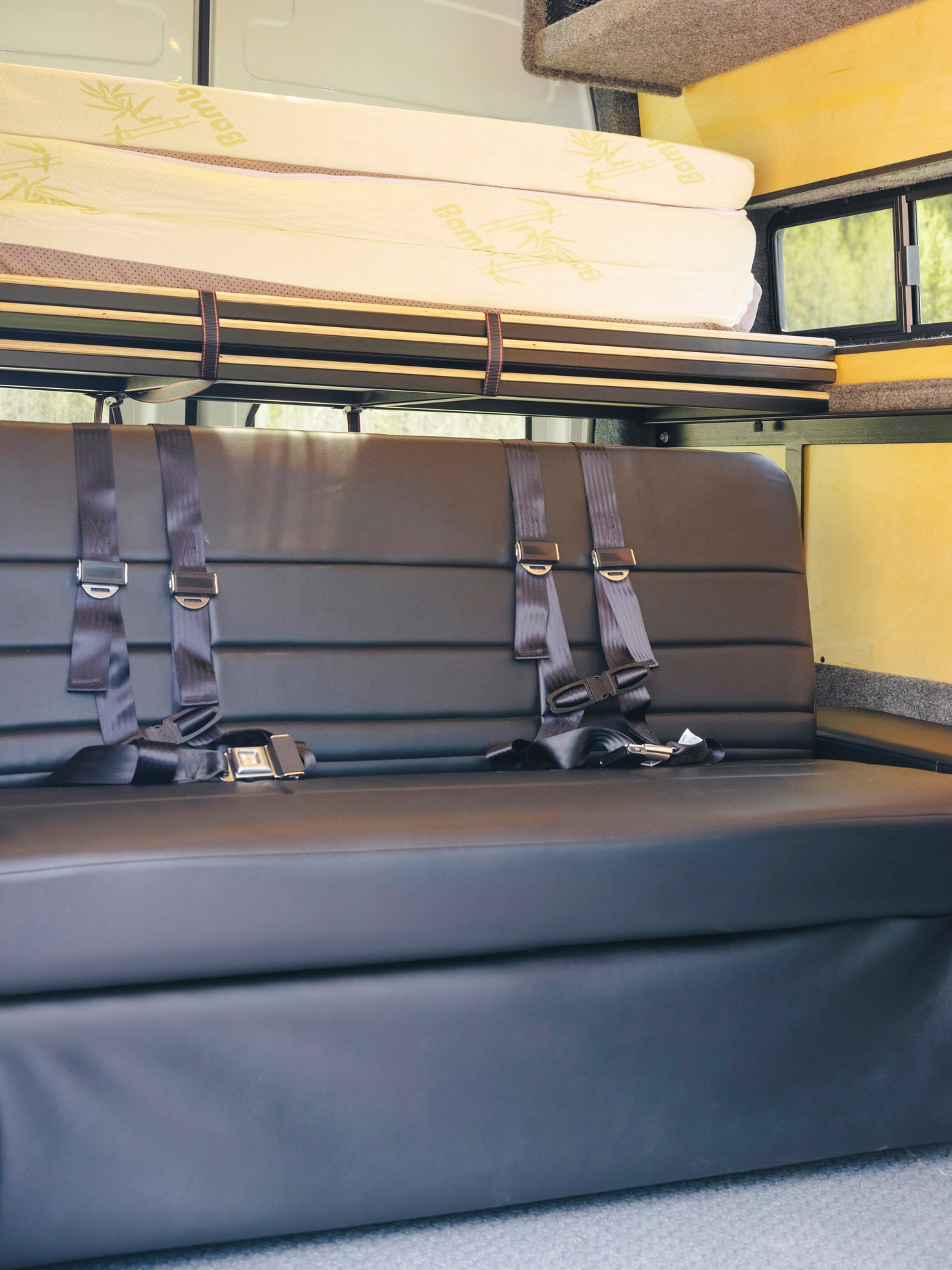 RV rental interior: Comfy black seats with seatbelts, overhead bed, and storage, ready for road trip adventures.
