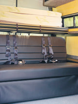 RV rental interior: Comfy black seats with seatbelts, overhead bed, and storage, ready for road trip adventures.