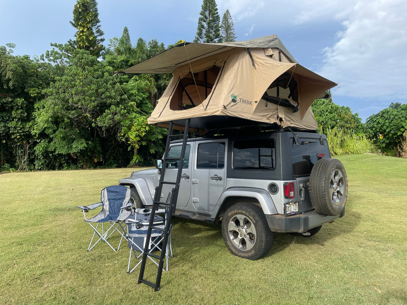 This versatile RV rental shows a silver Jeep with a deployed rooftop tent, ladder, chairs on grass, ready for camping.