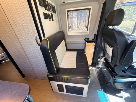 Interior of an RV rental, showcasing a bench seat, control panel, side window, and built-in storage.