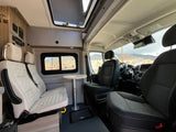 Spacious rv rental interior with comfortable seating, a table, and large windows revealing a mountain landscape.