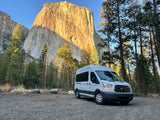 RV rental adventure: White van parked in Yosemite Valley, iconic El Capitan towering above, framed by tall pines.