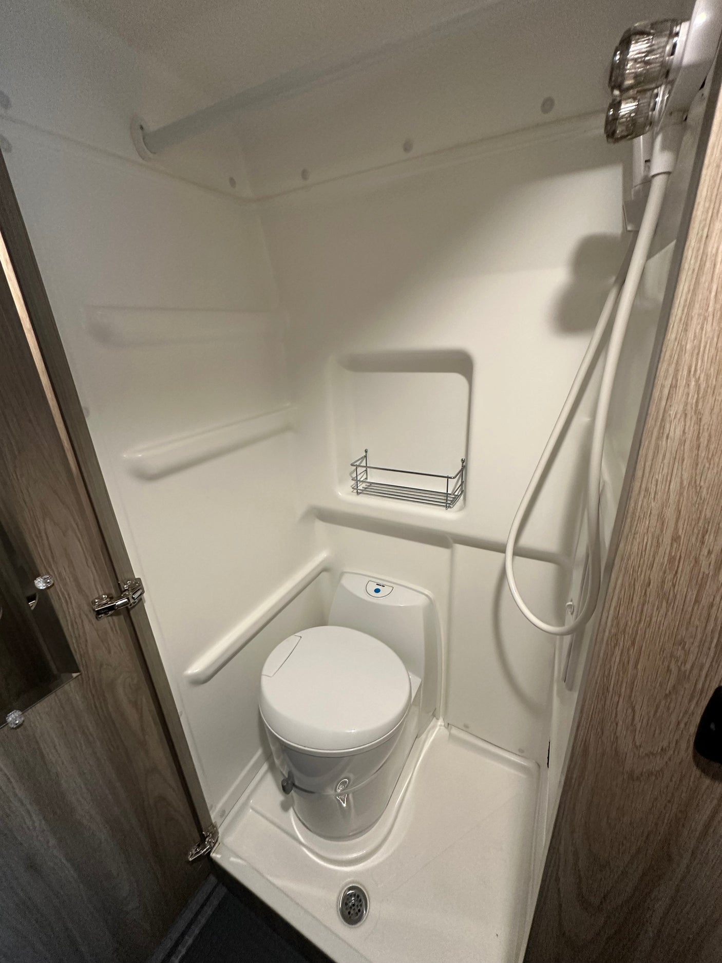 Clean, compact RV rental wet bath featuring a toilet, shower, and built-in shelving, ready for your trip.