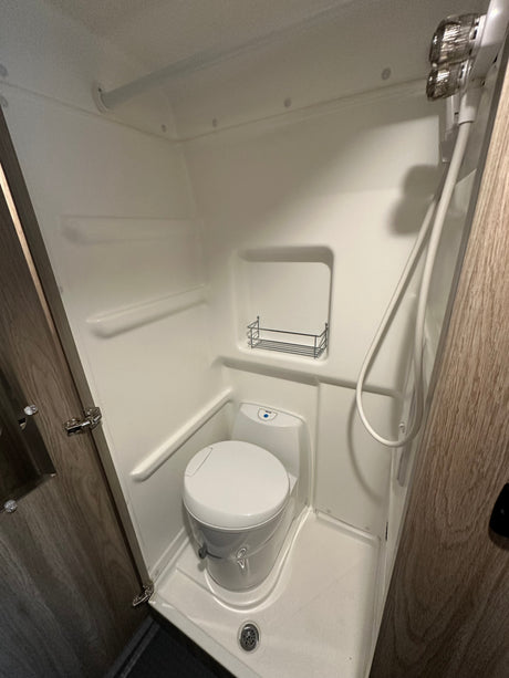 Clean, compact RV rental wet bath featuring a toilet, shower, and built-in shelving, ready for your trip.
