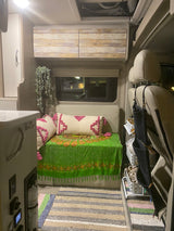 Explore this cozy RV rental interior: a vibrant bench with pillows, overhead wood cabinets, and smart storage for travel.