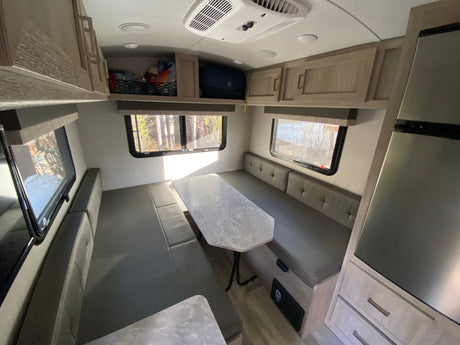 Modern RV rental interior: a bright dinette with gray benches, a table, and overhead storage. Ideal for comfortable travel.