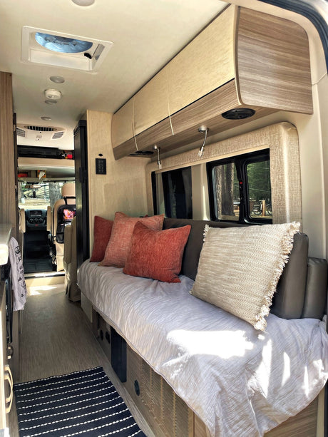 Inside a modern RV rental, featuring a cozy sofa/bed, overhead storage, and a well-lit living area, perfect for adventure.