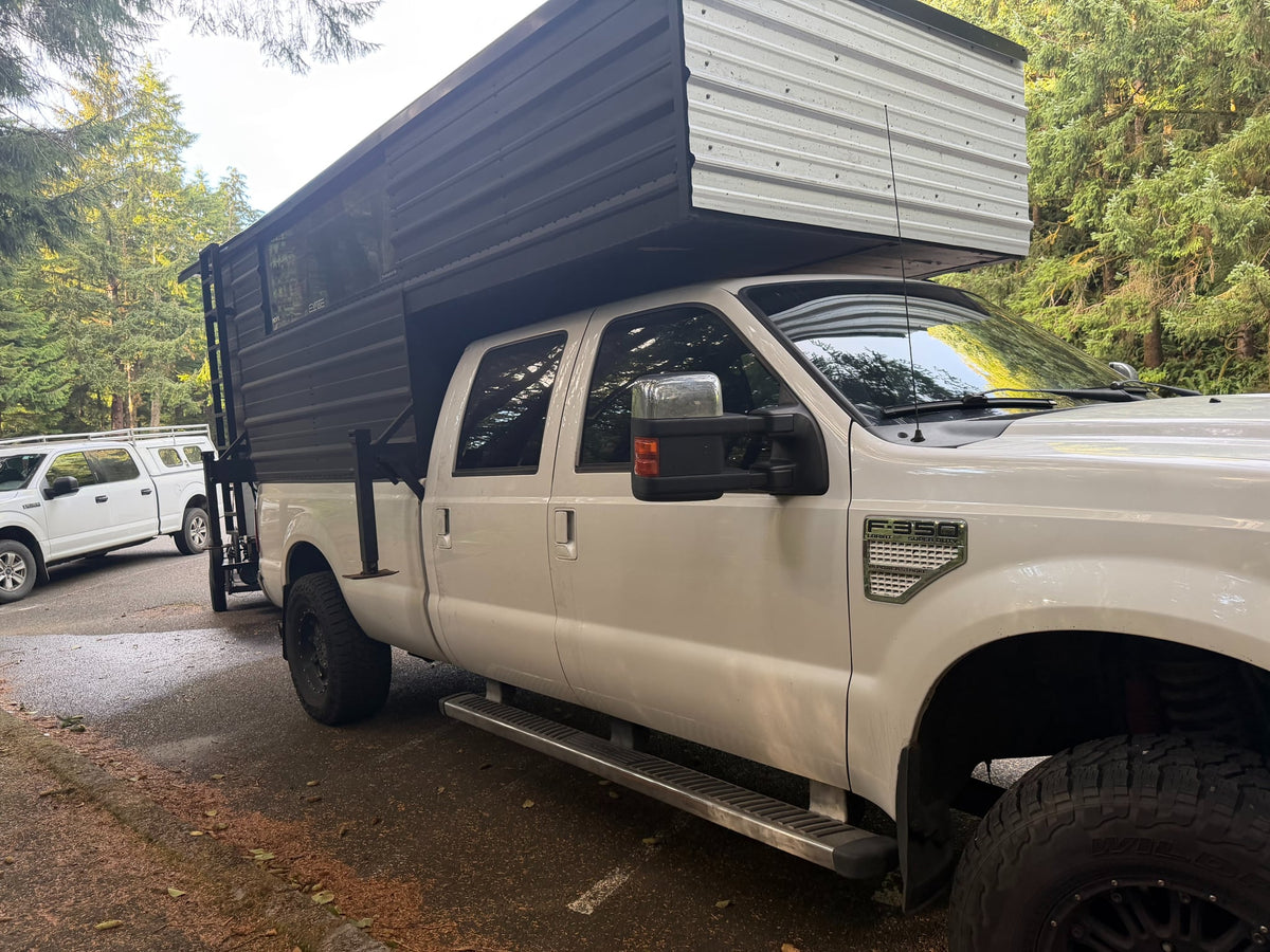 A white Ford F-350 Super Duty truck with a black/silver custom truck camper