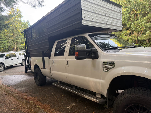 A white Ford F-350 Super Duty truck with a black/silver custom truck camper