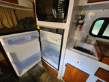 Explore this RV rental's galley: open fridge, microwave, sink, and mounted fire extinguishers, ready for your adventure.