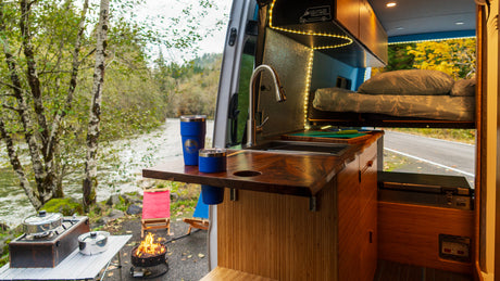 Cozy RV rental interior with kitchen, bed, and river view. Perfect for outdoor cooking by the campfire!