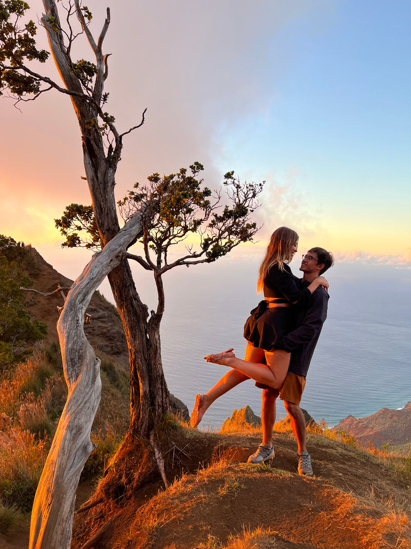 Couple embracing on a scenic cliff at sunset, overlooking the ocean with a unique tree. Ideal for your next RV rental journey. — photo 7
