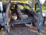 Inside an adventure-ready pickup truck for RV rental, all doors open, showing the spacious tan interior at a forest campsite.