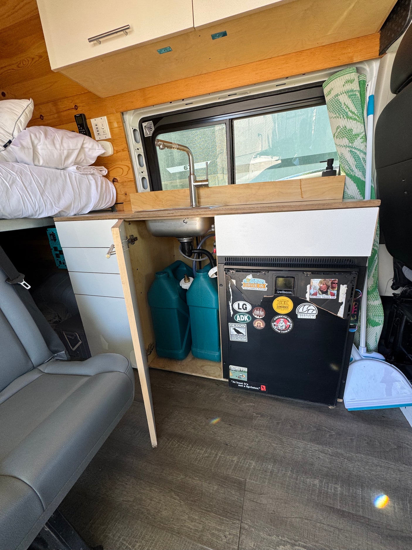Inside this RV rental camper van: A compact kitchen with a sink, faucet, and fridge, plus a cozy bed and storage.