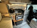 Cozy RV rental kitchen: compact two-burner stove with oven, sink, and mini-fridge. Perfect for your next road trip adventure.