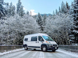 White RV rental van parked on a snowy road with beautiful snow-covered evergreen trees, ideal for winter adventures.