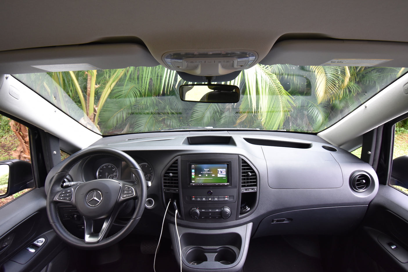Modern Mercedes-Benz RV rental van interior: dashboard, steering wheel, and infotainment system, with palm trees outside.