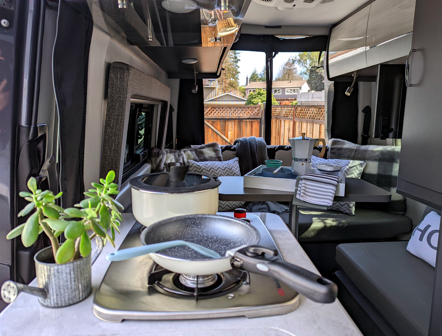 Cozy RV rental interior with a compact kitchen and dining area. Features include a stove, pan, pot, moka pot, and potted plant.