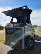 This grey adventure RV rental camper trailer is set up with a rooftop tent, ready for your outdoor escape.