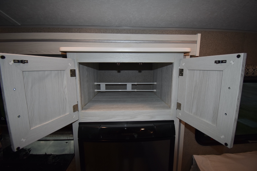 RV rental open cabinet: two white tension rods for secure storage, positioned above a black compact refrigerator.