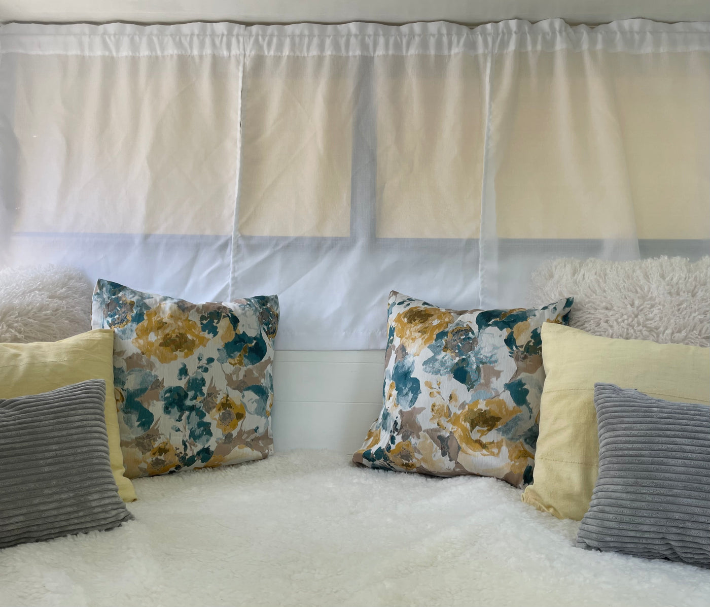 Cozy RV rental nook. Sheer curtains, plush white base, colorful floral, yellow, and grey pillows for comfort. — photo 10
